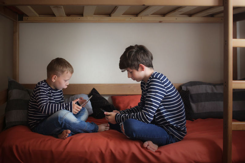 Brothers play gadgets on two bunk beds in a nursery, concept related relationships and gadgets, 