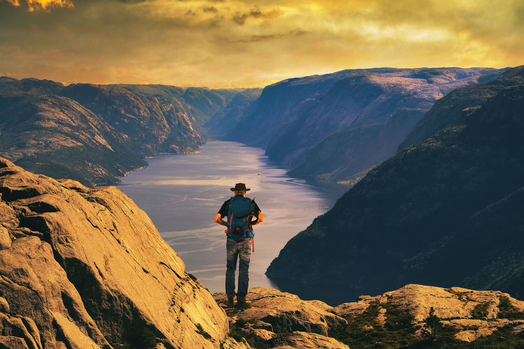 Man with hat and backpack on the mountains looking down to lysefjord