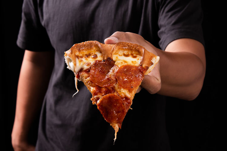 Close-up of hand holding pizza over black background