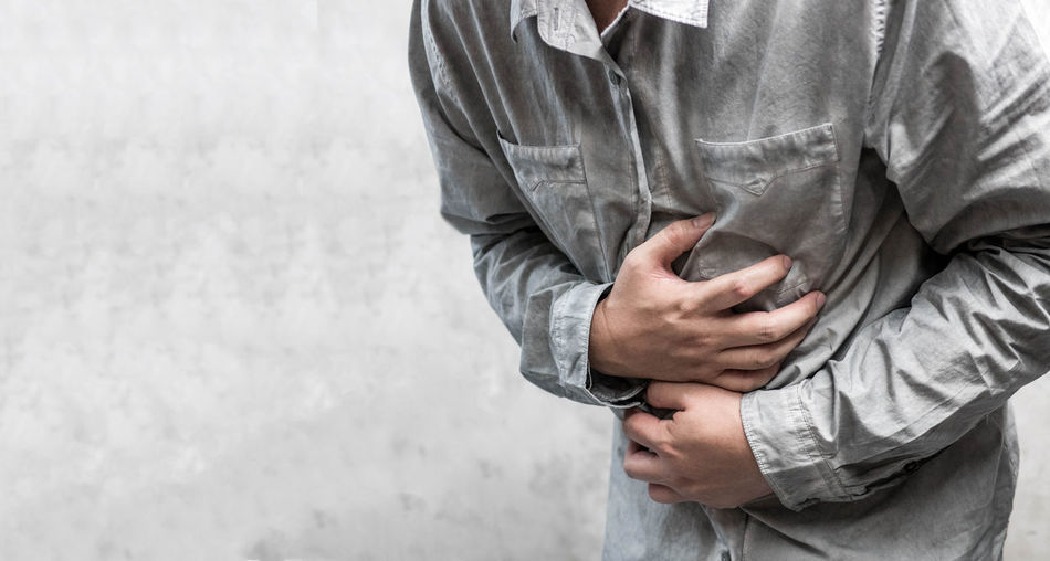 Midsection of man holding stomach while standing against wall