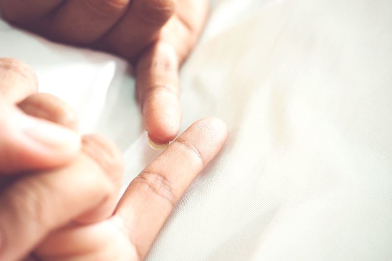Close-up of pinky fingers of man and woman on bed 