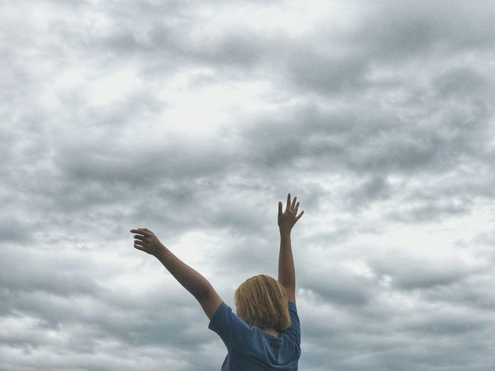 Low angle view of woman with arms raised against cloudy sky