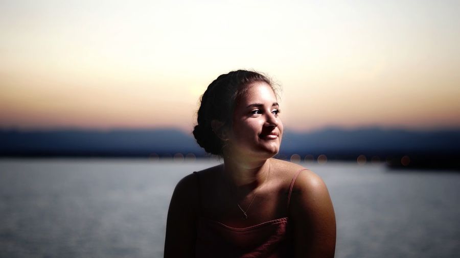 Portrait of young woman against sea during sunset