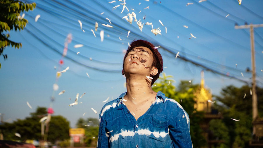 Petals falling on young man standing against blue sky