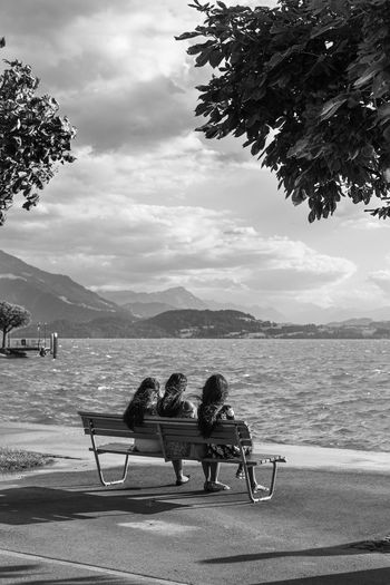People sitting on bench by sea against sky