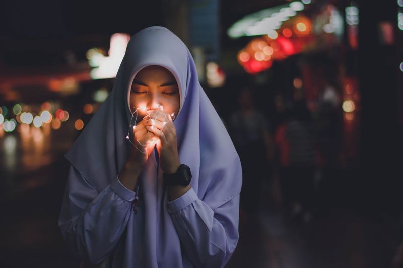 Woman wearing headscarf holding string light at night