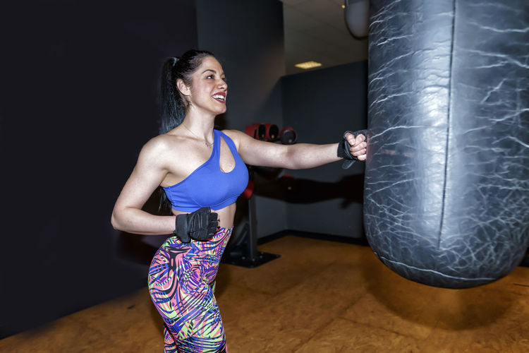 Smiling beautiful woman exercising with punching bag in gym
