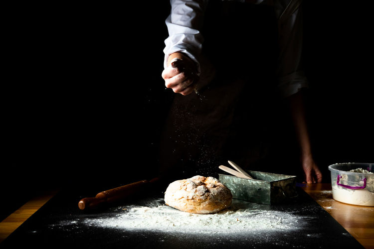 Rye bread and female chef hands with falling flour on black background. close-up