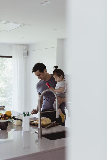 Father carrying male toddler while preparing food in kitchen