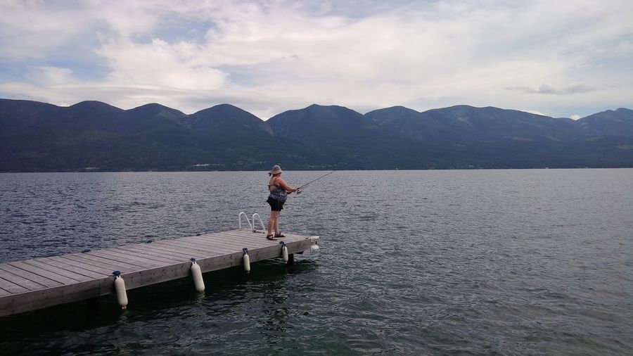 Woman fishing on lake dock, against sky