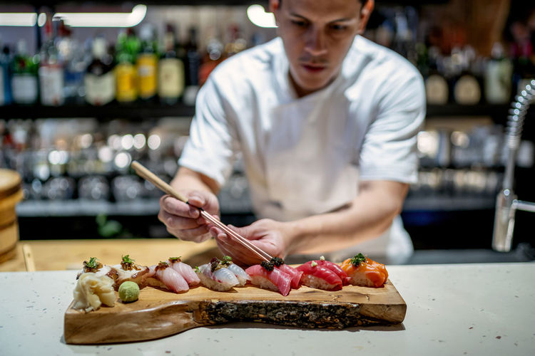 Male chef garnishing sushi on wooden serving tray in kitchen at restaurant