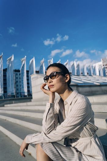 Young woman wearing sunglasses sitting in city against sky