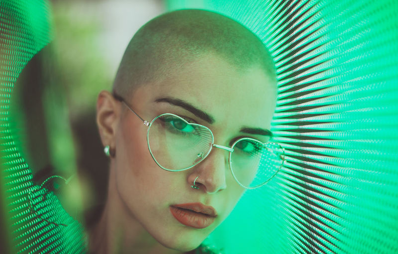 Portrait of young woman with shaved head standing against abstract backgrounds