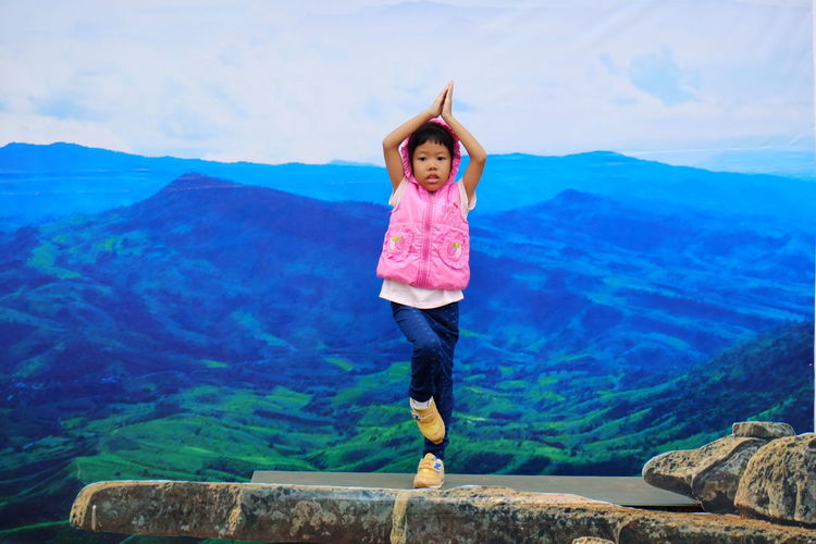 Portrait of girl doing yoga on rock against mountains