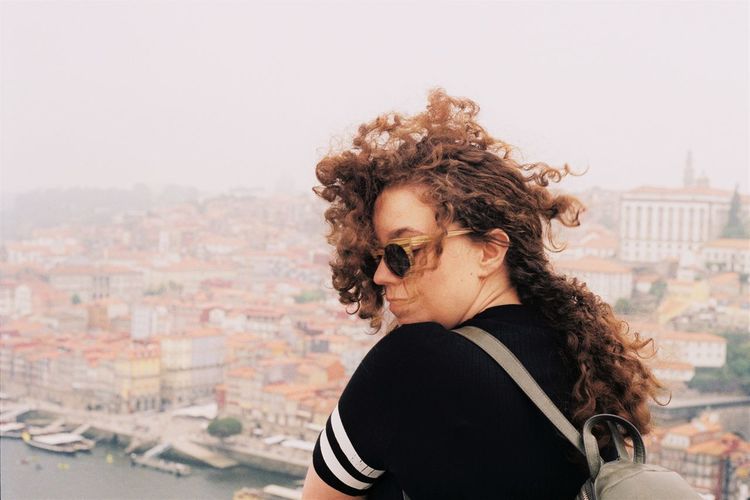 Portrait of girl with flowing curly hair standing against cityscape