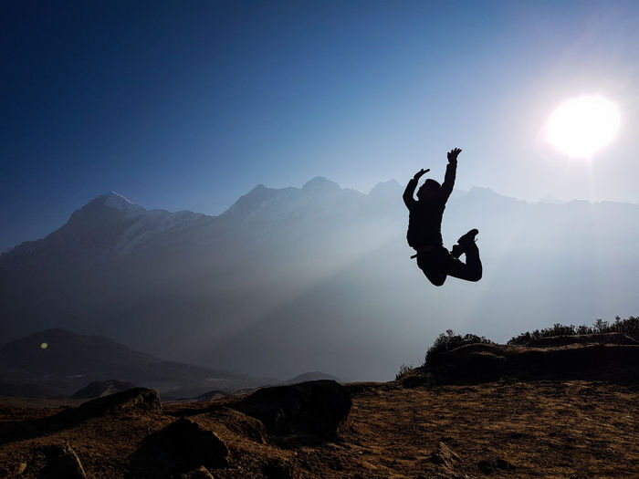 Silhouette man jumping on rock against mountain range