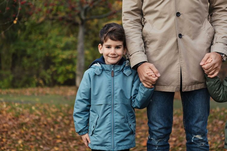 Portrait of smiling son holding hands with father while standing in park during autumn