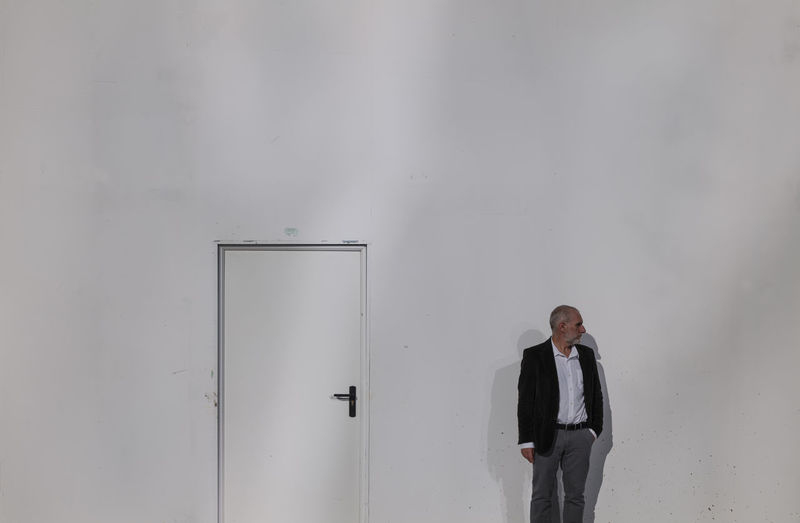 Portrait of adult man in suit against white wall with white door