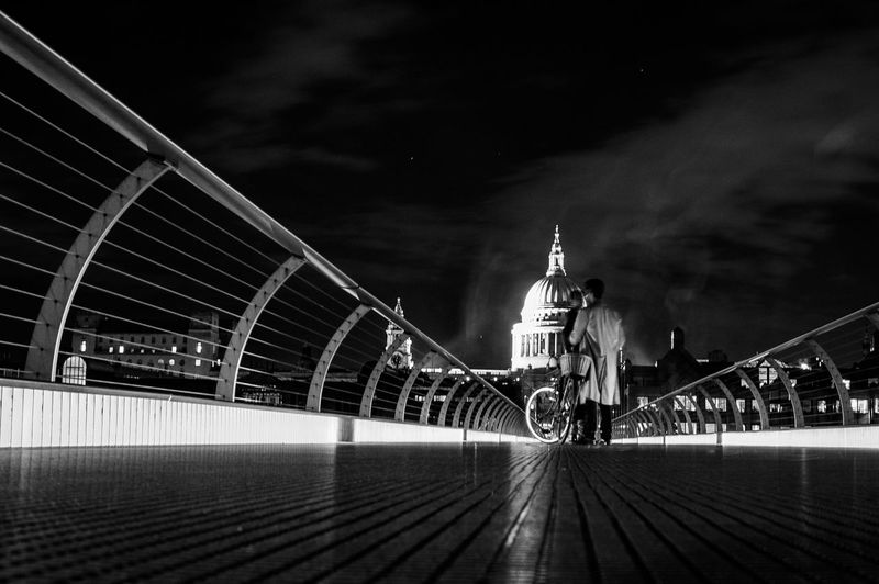 Man with bicycle standing on london millennium footbridge in front of st paul cathedral