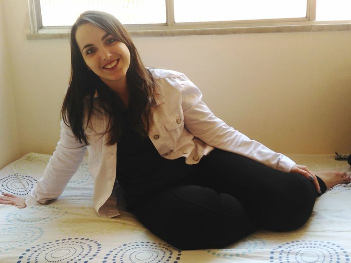 Portrait of smiling young woman sitting on bed at home