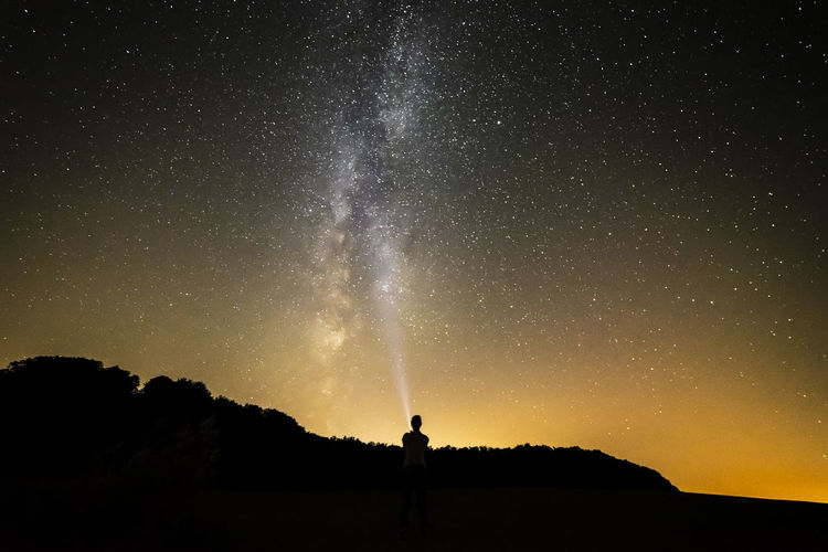 SILHOUETTE MAN STANDING AGAINST STAR FIELD AGAINST SKY AT NIGHT