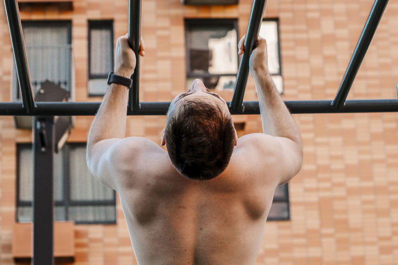 Rear view of shirtless man climbing outdoors