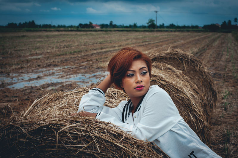 Thoughtful woman sitting on hay bale at field
