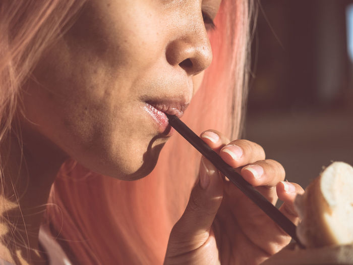 Close-up portrait of woman drinking through recyclable straw