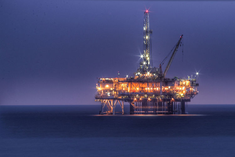 Illuminated drilling rig in sea against clear sky at night