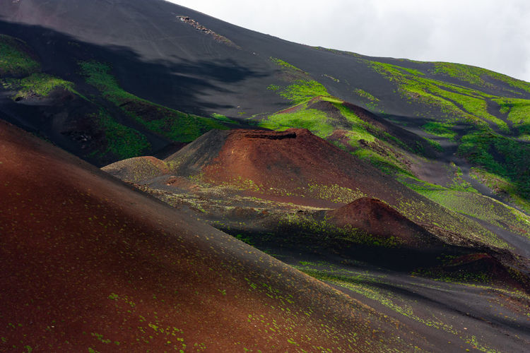 Breathtaking scenery of etna mountain. red volcanic sand and green vegetation with clouds shadows. 