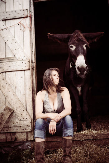 Young woman sitting in barn doorway with donkey