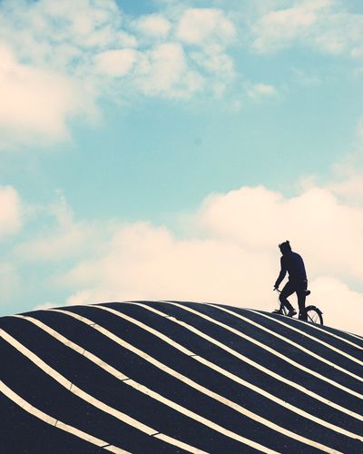 Silhouette man riding bicycle on road against sky