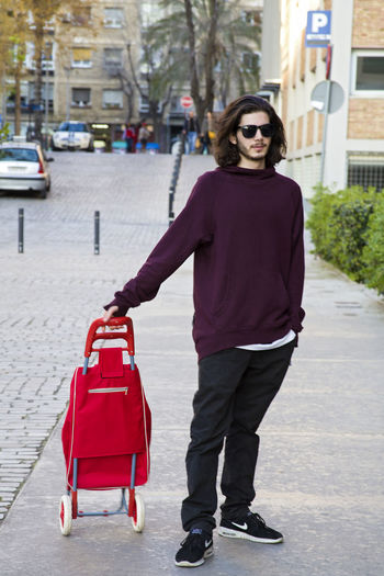 Young man with wheeled luggage standing on footpath