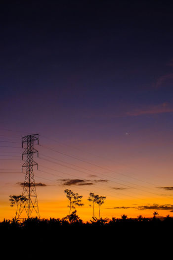 Silhouette electricity pylons against sky during sunset