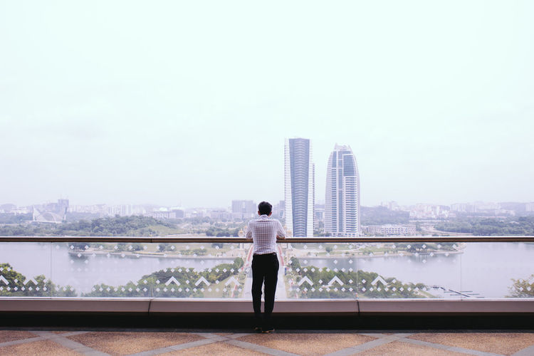 Rear view of man standing on railing against river
