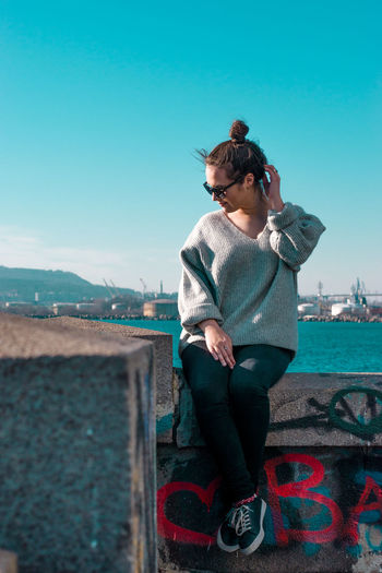 Young woman sitting on retaining wall against clear sky