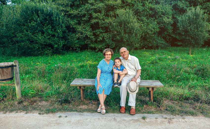 Full length portrait of family sitting on bench against trees