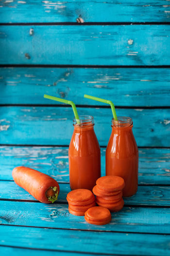 Freshly squeezed carrot juice on a blue background. healthy vegetable smoothie in glass bottles. 