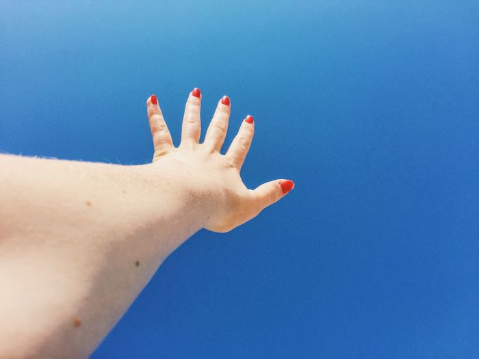 Close-up of woman hand against clear blue sky