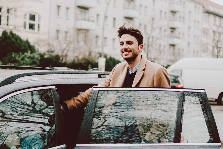 Happy young man entering wet car in city during rainy season