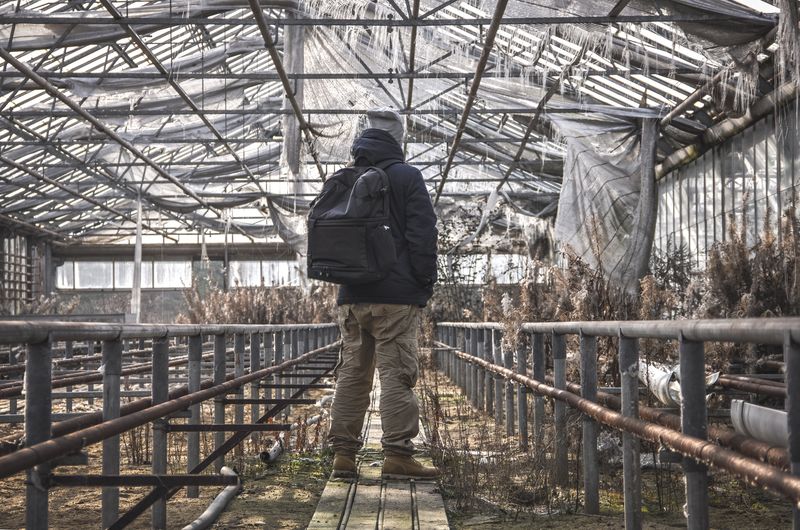 Rear view of man standing at abandoned metallic structure