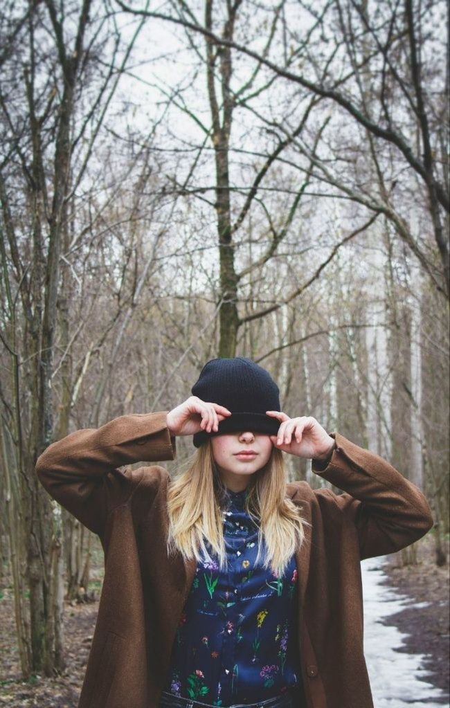 Beautiful young woman with hat over eyes against tree trunks