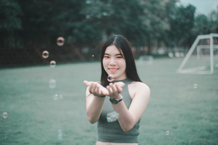 Portrait of smiling woman catching bubbles at park