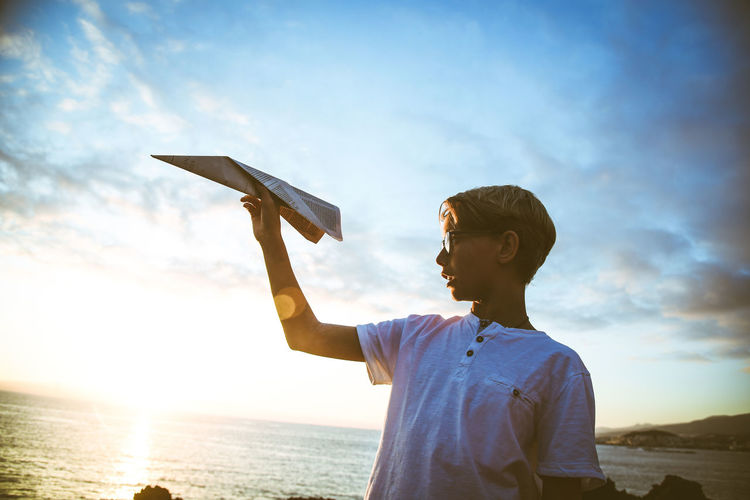 Low angle view of boy holding paper airplane against sky