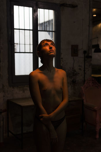 Woman looking away while standing against window