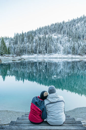 Rear view of couple sitting at lake against sky