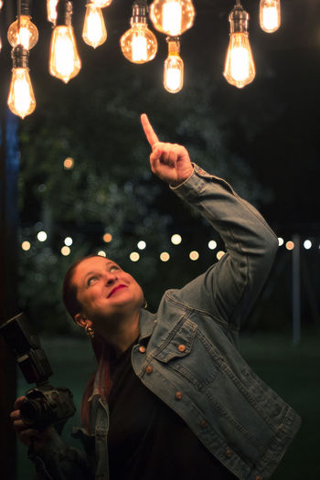Full length portrait of young woman holding illuminated lighting equipment at night