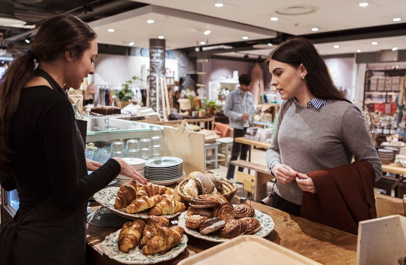 Saleswoman showing baked food to female customer at cafe