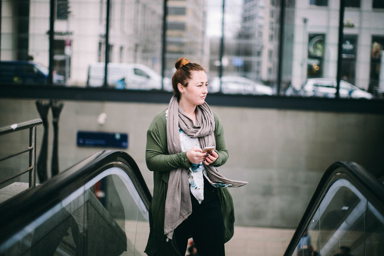 Young woman looking down while standing on railing in city