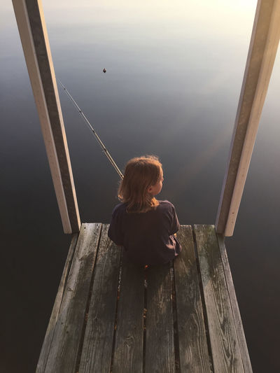 High angle view of girl fishing while sitting on pier over kentucky lake